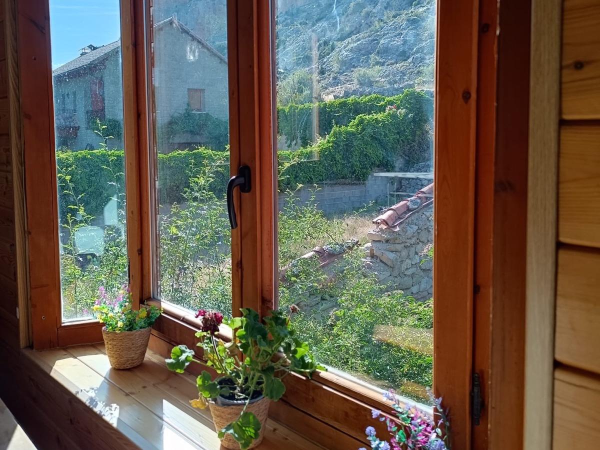 Ventana del comedor con macetas de flores en el alféizar y vistas al pueblo y a la pared rocosa