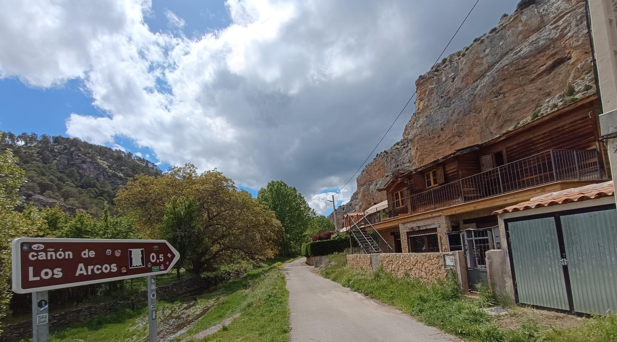 La casa de madera adosada a la pared rocosa, con el cartel del Cañón de Los Arcos en el inicio del sendero a unos metros